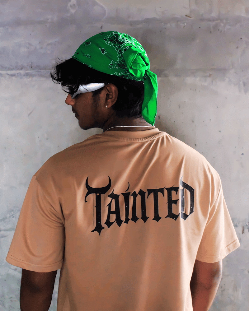 Man wearing a beige tainted flight graphic t-shirt with black gothic text on the back and a green bandana